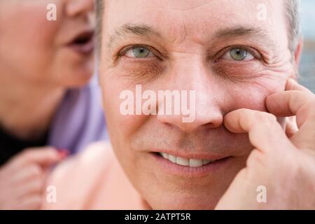 Porträt eines reifen Mannes mit Frau, die ihm ins Ohr flüstert. Stockfoto