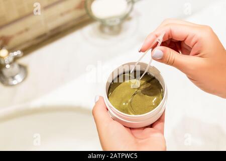 Weibliche Hände nehmen mit der Pinzette Augenflecken aus dem Behälter. Anti-Aging-Konzept. Stockfoto