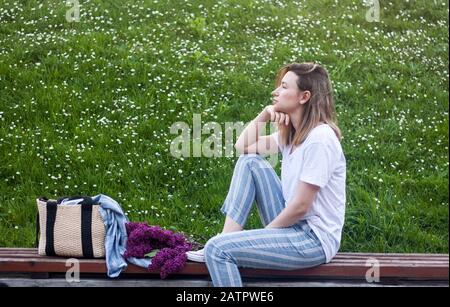 Frau sitzt im Park auf grünem Blumenhintergrund, Lifestyle-Konzept im Frühling, ungezwungener moderner Stil Stockfoto