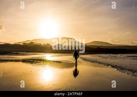 Ardara, County Donegal, Irland. Februar 2020. Low Winter Sonnenschein Silhouetten ein Wanderer auf dem "Wild Atlantic Way" Strand. Stockfoto