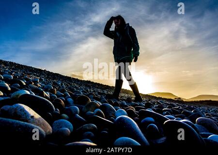 Ardara, County Donegal, Irland. Februar 2020. Low Winter Sonnenschein Silhouetten ein Wanderer auf dem "Wild Atlantic Way" Strand. Stockfoto