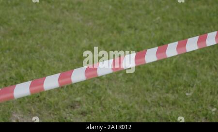 Rotes und weißes temporäres Umfassungsband auf dem Hintergrund von grünem Gras. Stockfoto