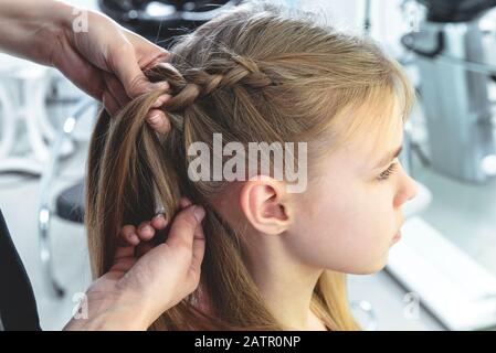 Friseursalon verwebt einem blonden Mädchen der Preteen ein Geflecht Stockfoto