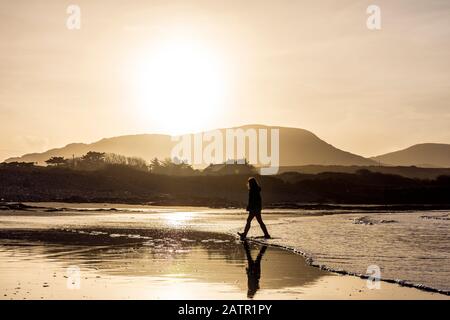 Ardara, County Donegal, Irland. Februar 2020. Low Winter Sonnenschein Silhouetten ein Wanderer auf dem "Wild Atlantic Way" Strand. Stockfoto