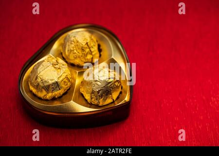 Goldfarbene Luxus-Schokolade in Herzform, isoliert auf rotem Hintergrund mit Kopierraum. Valentinstag Geschenkkonzept für Poster, Banner, grafische Ressourcen, Stockfoto
