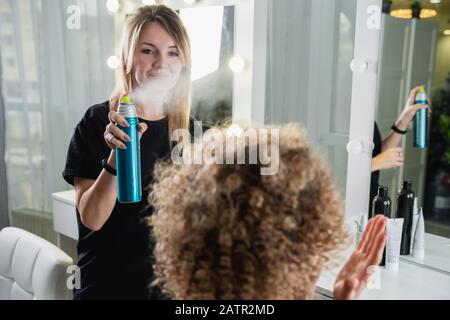 Nahaufnahme der Hände des Friseursalons mit Haarspray auf den Haaren des Kunden im Salon Stockfoto