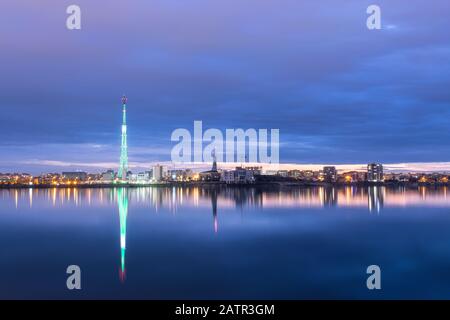 Langzeitfoto eines schönen Sonnenuntergangs am Lacul Morii Lake mit städtischen Gebäuden im Hintergrund und einem Turm, der wie ein Weihnachtsbaum aussieht - La Stockfoto