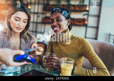 Glückliche Freunde, die mit Kreditkarte zahlen und kontaktlose Zahlungen in einem Restaurant leisten. Stockfoto