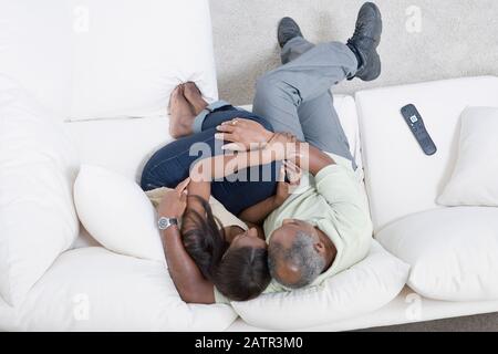 Blick aus dem hohen Winkel auf ein Paar mittleren Alters, das auf einem sitzt Couch umarmt sich gegenseitig Stockfoto