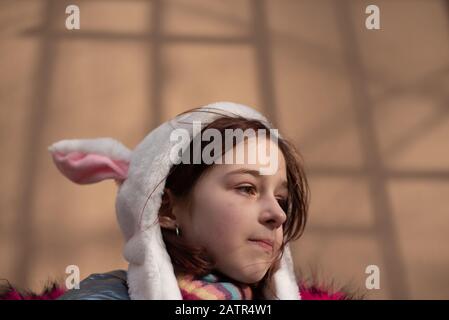 Süßes kleines Mädchen in der Kapuze mit Ohren, Mädchen in einer Huth-Bunny-Straße. Schöne junge süße Frau in blauem veganen und Kunstfellmantel posiert auf dem städtischen Bac Stockfoto