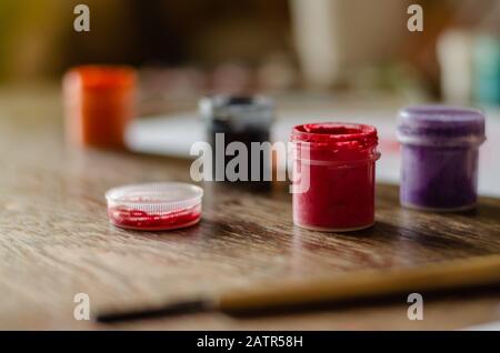 Gouache-Farben und eine Bürste zum Malen im Vordergrund. Verschwommener Hintergrund. Das Konzept der Inspiration und Kreativität. Nahaufnahme. Selektiver Fokus. E Stockfoto
