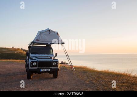 Geländewagen mit Allradantrieb und Zeltlager auf dem Dach entlang der Ostsee bei Sonnenaufgang im Sommer, Skåne/Scania, Schweden Stockfoto