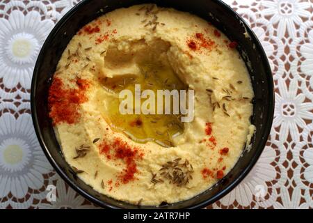 Hummus, Kichererbsendip, mit Gewürzen in einem schwarzen Teller auf dem Tisch. Draufsicht. Traditioneller klassischer Hummus. Vegetarisches Gericht. Stockfoto
