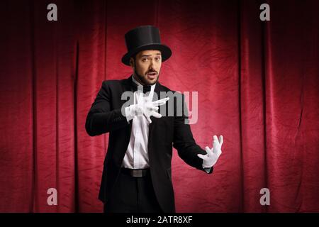 Männlicher Zauberer führt einen Trick mit Hut auf einer Bühne mit rotem Vorhang durch Stockfoto