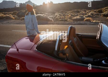 Frau, die wunderschöne felsige Landschaften genießt, während sie mit einem Auto während eines Sonnenuntergangs am Straßenrand der Wüste steht. Reisen im vulkanischen Tal auf Teneriffa Stockfoto