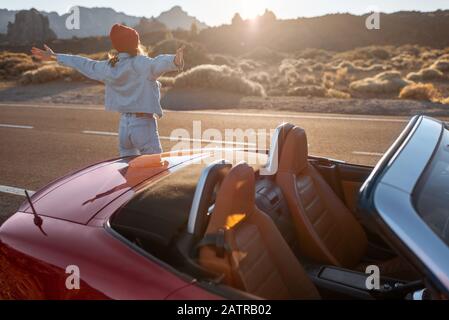 Frau, die wunderschöne felsige Landschaften genießt, während sie mit einem Auto während eines Sonnenuntergangs am Straßenrand der Wüste steht. Reisen im vulkanischen Tal auf Teneriffa Stockfoto