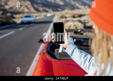 Frau, die mit dem Auto auf dem vulkanischen Tal unterwegs ist, hält Smartphone mit leerem Bildschirm, um Paste am Straßenrand zu kopieren Stockfoto