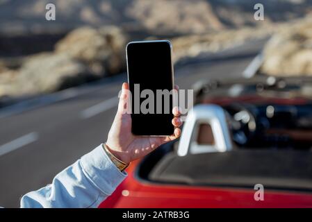 Frau, die mit dem Auto auf dem vulkanischen Tal unterwegs ist, hält Smartphone mit leerem Bildschirm, um Paste am Straßenrand zu kopieren Stockfoto