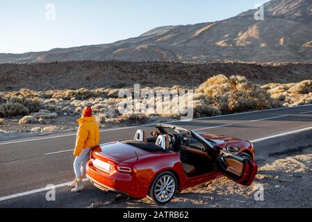 Frau, die wunderschöne felsige Landschaften genießt, während sie mit einem Auto während eines Sonnenuntergangs am Straßenrand der Wüste steht. Reisen im vulkanischen Tal auf Teneriffa Stockfoto