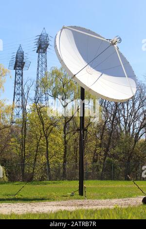 Satellitenschüssel mit elektrischen Stromübertragungstürmen im Hintergrund Stockfoto