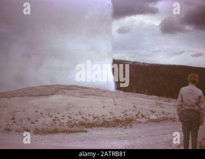Nakuläres Foto, aufgenommen auf einer analogen 35-mm-Filmtransparenz, vermutet, dass es Touristen mit Geysir, 1965, abbildet. Zu den wichtigsten Themen/Objekten gehören Himmel, Geysir, Landschaft und Natur. () Stockfoto