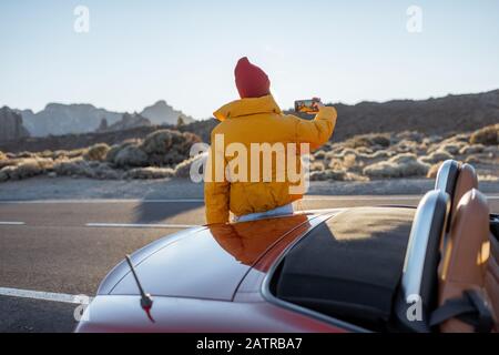 Frau, die wunderschöne vulkanische Landschaften genießt und während eines Sonnenuntergangs am Straßenrand telefoniert. Reisen im Wüstental auf Teneriffa Stockfoto
