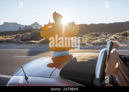 Frau, die wunderschöne vulkanische Landschaften genießt und während eines Sonnenuntergangs am Straßenrand telefoniert. Reisen im Wüstental auf Teneriffa Stockfoto