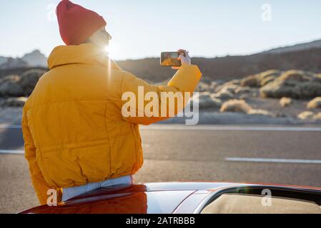 Frau, die wunderschöne vulkanische Landschaften genießt und während eines Sonnenuntergangs am Straßenrand telefoniert. Reisen im Wüstental auf Teneriffa Stockfoto