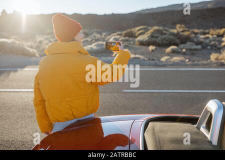 Frau, die wunderschöne vulkanische Landschaften genießt und während eines Sonnenuntergangs am Straßenrand telefoniert. Reisen im Wüstental auf Teneriffa Stockfoto