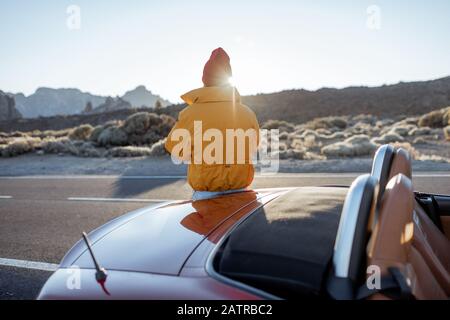 Frau, die wunderschöne vulkanische Landschaften genießt und während eines Sonnenuntergangs am Straßenrand telefoniert. Reisen im Wüstental auf Teneriffa Stockfoto