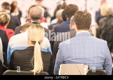 Business man und blonde Frau mit langen Haaren und Leuten, die auf der Konferenz oder auf dem Training im Saal zuhören Stockfoto