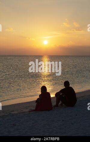 Romantischer Urlaub - ein Paar sitzt an einem Strand und beobachtet den Sonnenuntergang über dem Indischen Ozean, den Malediven, Asien Stockfoto