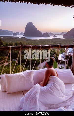 Junge Männer im Bett aufwachen mit Blick über die Phangnga-Bucht bei Sonnenaufgang Thailand in der Dschungel Holzbambushütte in den Bergen Stockfoto