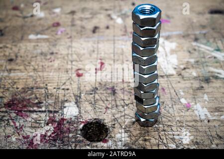 Turm aus verschiedenen Sechskantmuttern aus Metall auf Holzwerkbank mit fleckiger Grunge, strukturierte Oberfläche. Stockfoto