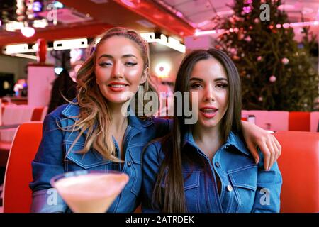 Coole Damen mit hellem Make-up und stylischen Frisuren, die im Restaurant sitzen und eine gute Zeit zusammen haben. Jeans-Hemden tragen. Beste Freunde Stockfoto