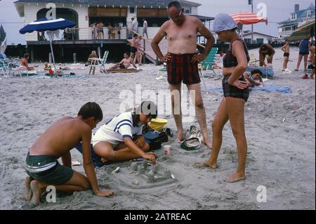 Nakuläres Foto, aufgenommen auf einer analogen 35-mm-Filmtransparenz, glaubte, Menschen tagsüber am Strand abzubilden, 1970. Zu den wichtigsten Themen/Objekten, die erkannt wurden, gehören Strand und Gruppe. () Stockfoto