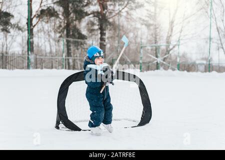 Kleiner lustiger Junge mit ihrer Mutter, die im Park Schlittschuhlaufen macht. Spielen Sie Eishockey mit Stick und Tor. Im Freien. Wintersport Stockfoto