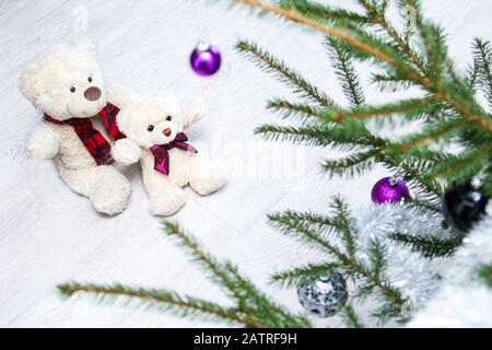 Zwei niedliche Teddybären sitzen am weihnachtsbaum und beobachten, wie schön es ist. Stockfoto