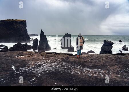 Frau, die auf der Klippe steht und die Macht des Ozeans auf dem Seeast reykjanesviti in Island beobachtet Stockfoto
