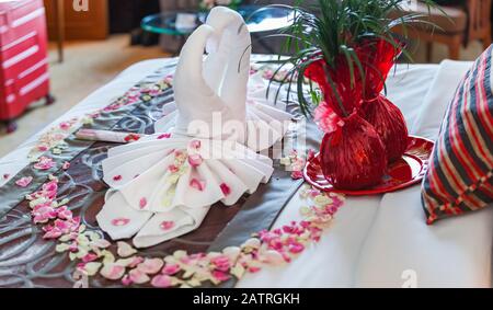 Romantisches Schlafzimmer Innenraum, Küssen Swan Origami Handtücher und streute frische Rosa Weiße Rose Blumenblätter Dekoration auf dem Bett für frisch verheiratete Paare. Weddin Stockfoto