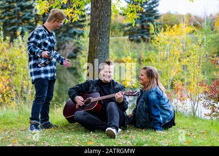 Ein junger Mann mit Down-Syndrom spielt ein Tamburin, während sein Vater Gitarre spielt und seine Mutter mitsingt, während sie sich gegenseitig in Gesellschaft genießt ... Stockfoto