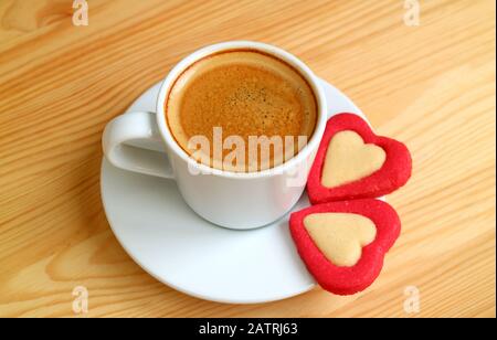 Eine Tasse Espresso-Kaffee mit einem Paar von roten, Herzförmigen Plätzchen auf dem Holztisch für das Valentinstag Konzept Stockfoto