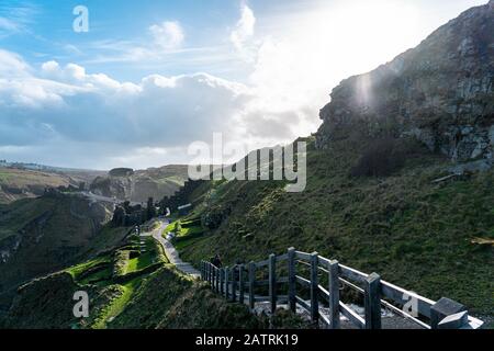 Führen Sie mit der Brücke im Hintergrund bis zur Burg Tintagel. Ein Lichtnebel bedeckt die Hügel von Tintagel. Ein wunderschöner Sonnenaufruß spuckt auf dem Boden. Stockfoto