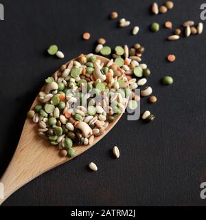 Mischen Sie getrocknete Hülsenfrüchte in einem Holzlöffel, der auf dunklem Hintergrund isoliert ist. Draufsicht. Stockfoto