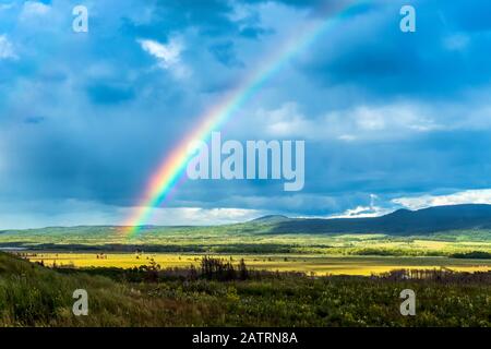 Regenbogen über Tal mit sanften Hügeln im Hintergrund und dunklen Wolken, Waterton Lakes National Park; Waterton, Alberta, Kanada Stockfoto