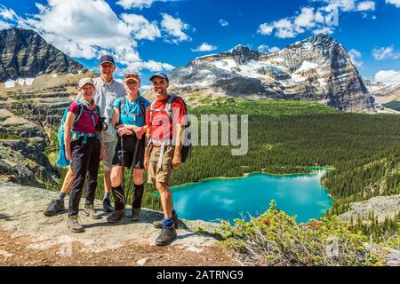 Zwei Paare Wanderer stehen auf felsigen Kamm mit blauen alpinen See und Berge in der Ferne mit blauen Himmel und Wolken, Yoho Nationalpark Stockfoto