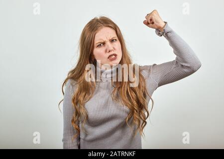 Frau im grauen Pullover eine irritierte wütende Dame schüttelt ihre Faust im Zorn Stockfoto