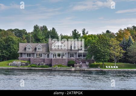 Tagsüber in einem grasigen Gebiet an der Küste eines Sees bauen und von Bäumen umgeben. Real-State-Konzept. Tausende Inseln. Ontario, Kanada. Stockfoto