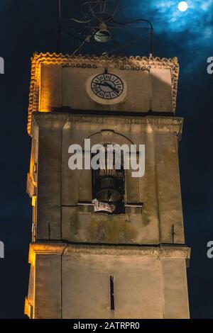 Der mittelalterliche Kirchturm mit einer Uhr und einer Glocke nachts im Dunkeln bei einem Vollmond in einem französischen Dorf (10. Januar 2020) Stockfoto