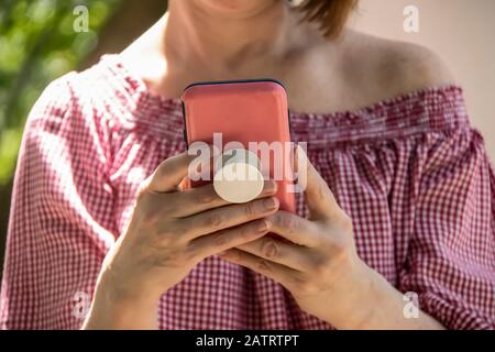 Nahaufnahme der Frau, die in einem rosafarbenen Gehäuse mit Griff auf dem Rücken von einem Handy hält und liest - von der Schulterbluse und kurzen Haaren - selektiver Fokus Stockfoto